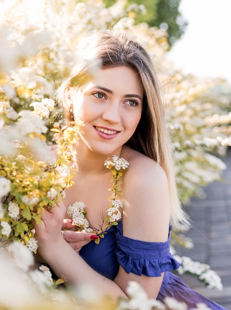 Sensual calm portrait of beautiful hipster woman in blooming bush with white flowers of spirea. Copy space. Stylish blonde woman in blue dress in garden