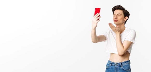 Sensual gay man in crop top taking selfie on smartphone sending air kiss at phone camera and close e