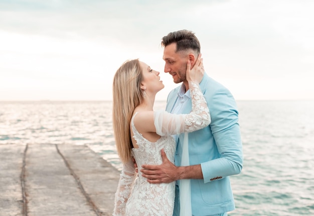 Sensual newlyweds stand holding hands on the background of the blue sea Wedding walk on a sand beach In the background blue sky