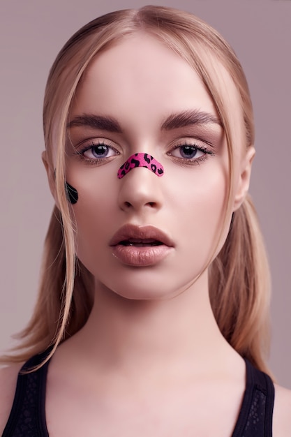 Sensual portrait of beautiful blonde girl with glamour plasters on her face posing at studio