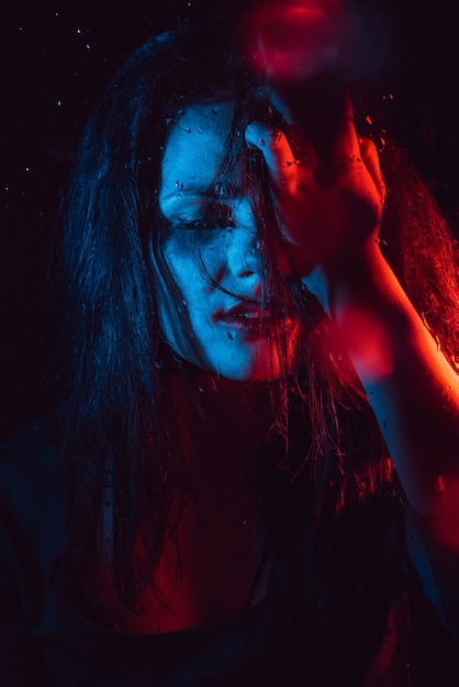 Sensual portrait of sad melancholic lonely girl behind glass with raindrops