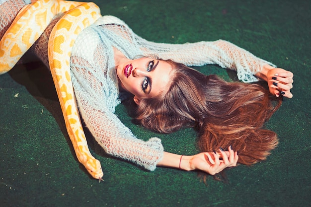 Sensual woman relax with albino python Snake crawl on woman with long hair Beauty model with makeup face and yellow serpent Danger temptation and desire concept