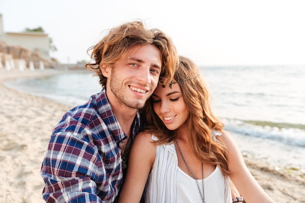 Sensual young couple sitting and smiling on the beach