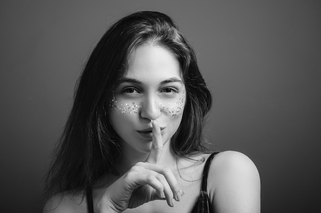 Sensual young woman Cunning look Shush gesture Beautiful female with finger at lips Black and white portrait