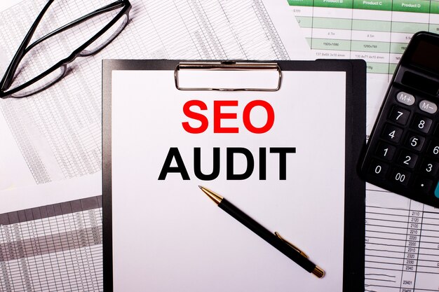 SEO AUDIT is written on a white sheet of paper, near the glasses and the calculator.