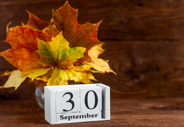 September 30 on a wooden calendar and an autumn bouquet of maple colored leaves. date of the autumn month.The concept of Golden autumn.