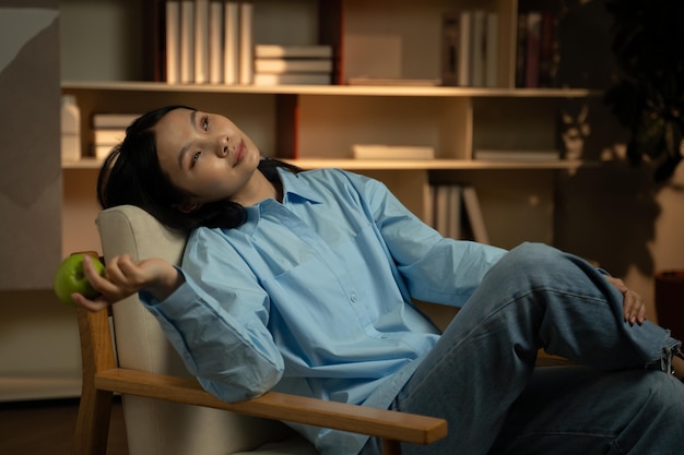 Photo serene asian woman relaxing with green apple in cozy evening home setting