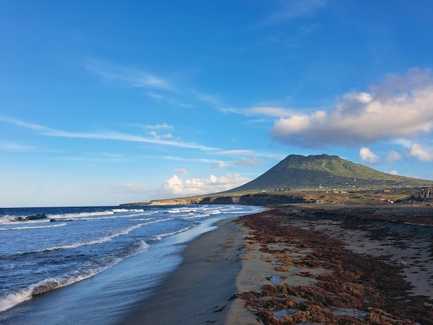 A serene beach with waves lapping at the shore framed by a lush mountain against a clear blue sky