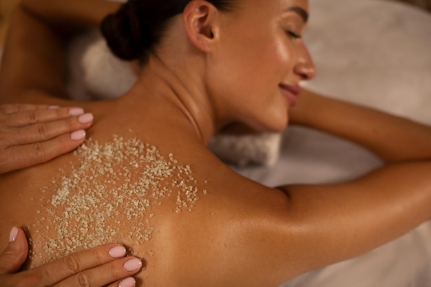 Photo serene woman deeply relaxing as spa professional applying an exfoliating treatment to her back