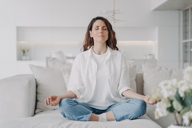 Photo serene woman practicing yoga meditation relaxing for stress relief on comfortable sofa at home