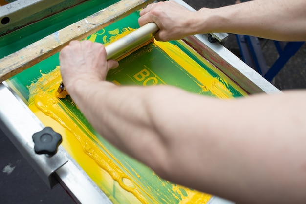 Serigraphy silk screen print process at clothes factory. Frame, squeegee and plastisol color paints