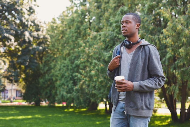 Serious african-american student with take away coffee in park outdoors, having rest in campus. Education concept, copy space