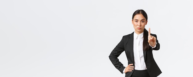 Serious angry asian businesswoman making restriction give warning sign Displeased saleswoman showing stop shaking finger as scolding someone forbid action white background