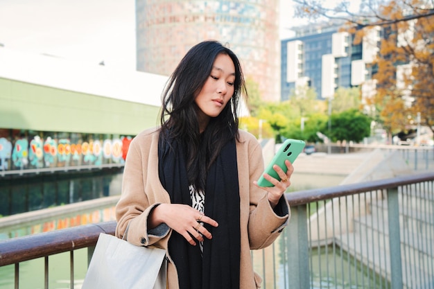 Serious asian business young woman watiching in the cell phone app a message text outdoors Unhappy chinese girl reading news on the smartphone