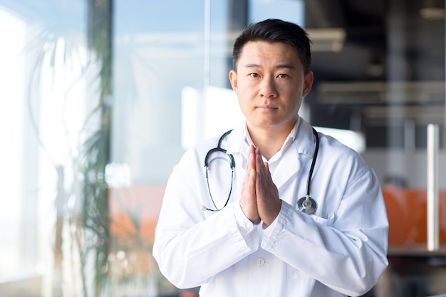 Serious asian doctor looking at webcam listening to patient interlocutor online man working remotely from clinic