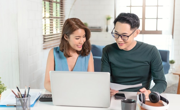 Serious Asian husband checking analyzing statement utilities bills sitting together at home.