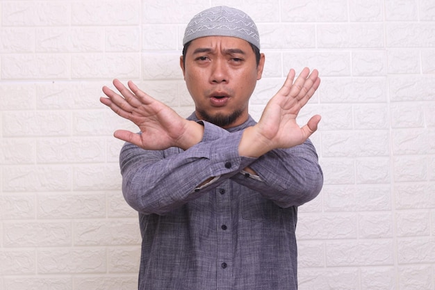 Serious Asian muslim man crossing hands gesturing warning or prohibition against white background