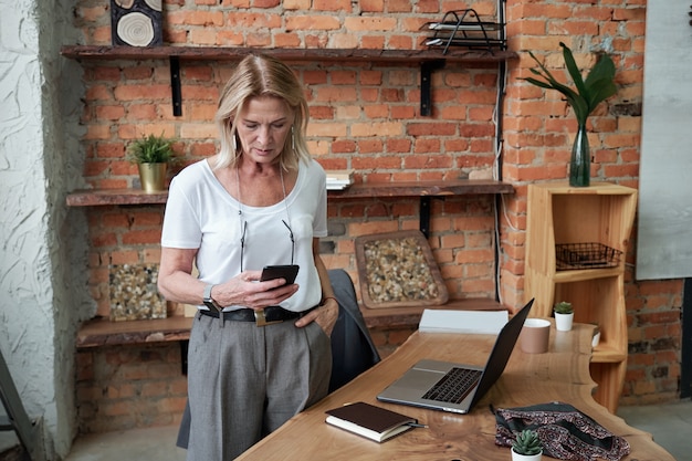 Photo serious attractive lady boss checking phone message while standing in modern office