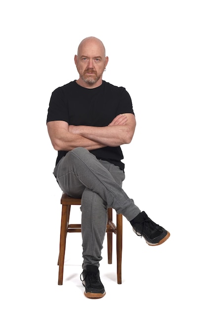 Serious bald man with sportswear sitting on white background