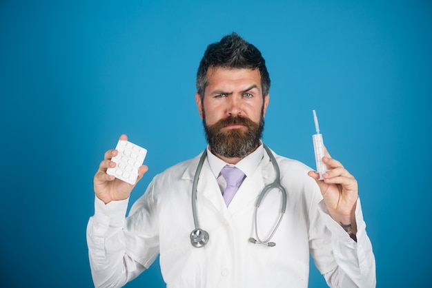 Serious bearded intern physician doctor in uniform and stethoscope on neck holds pills and syringe