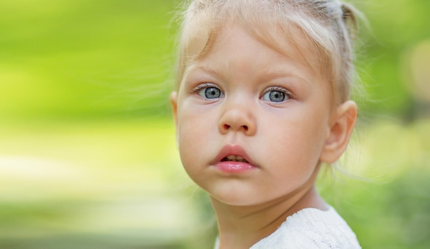 Serious beautiful little girl looking at camera on the green blurred background