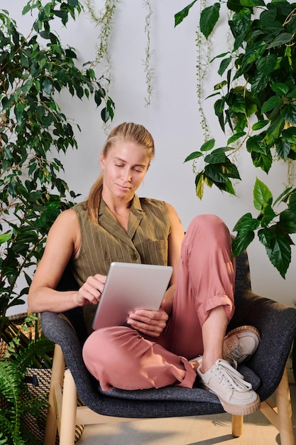 Serious blond female manager in casualwear scrolling in tablet in office