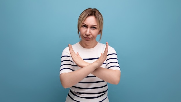 Serious blond girl showing cross gesture with hands on blue background with copy space