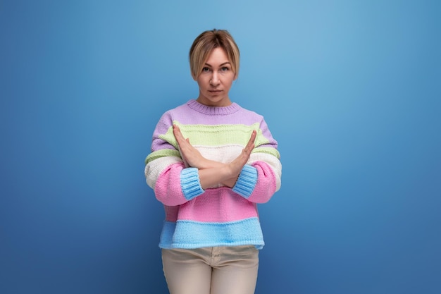 Serious blond woman in casual outfit showing consent gesture on blue background with copy space