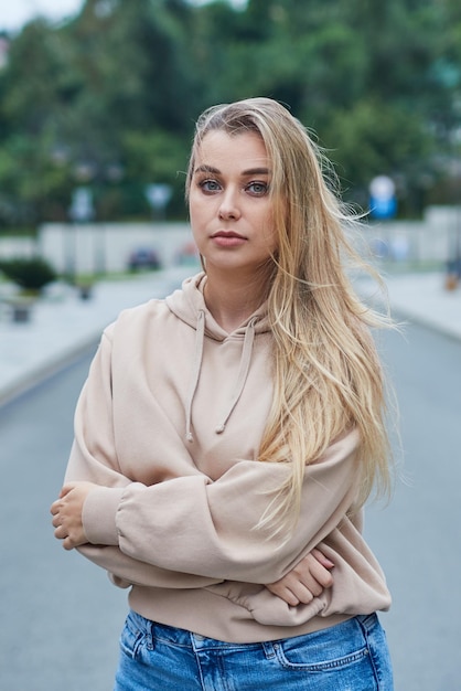 Serious blonde teenager stands against the backdrop of the city with her hands clasped