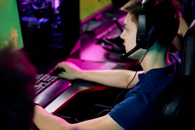 Serious boy in headset with microphone sitting at table and playing video game in computer club