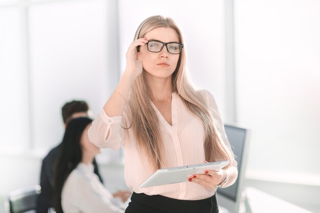 Serious business woman with digital tablet standing near office desk