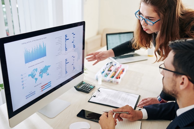 Serious businessman and businesswoman discussing charts and diagrams with statistics on computer screen