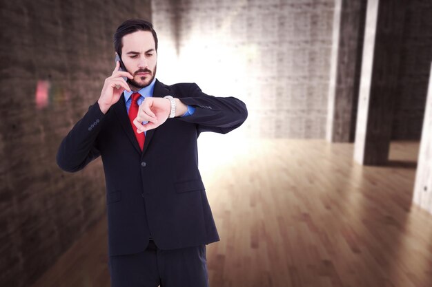 Serious businessman checking the time while on the phone against abstract room