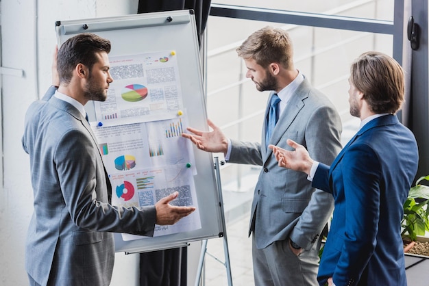 Serious businessman standing near whiteboard with business charts and discussing project