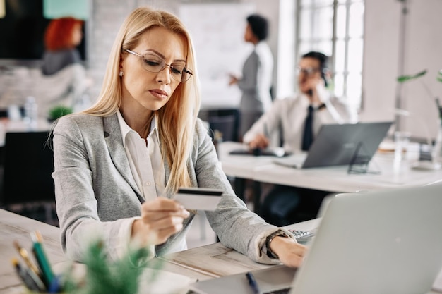 Serious businesswoman making payments online with a credit card while sitting at her desk in the office