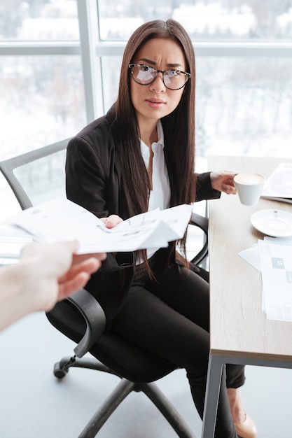 Serious businesswoman receiving documents and drinking coffee at the table