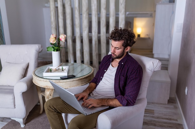 Photo serious bussines man with serious face sitting at home and using laptop for his project. freelance working from home concept business man at home checking statistics on mobile phone and laptop