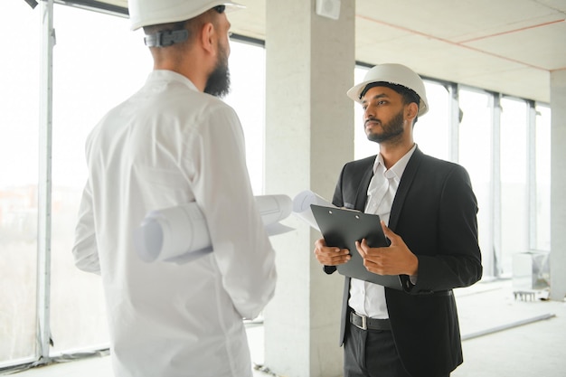 Photo serious busy young attractive arabic industrial engineer in hard hat with project drawings in factory interior professional and industry builder architect job worker checking work at plant indoor