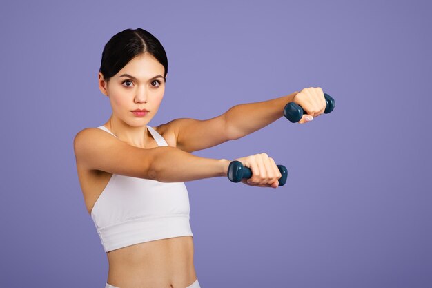 Photo serious caucasian slim woman in sportswear doing exercises with hand dumbbells looking at camera