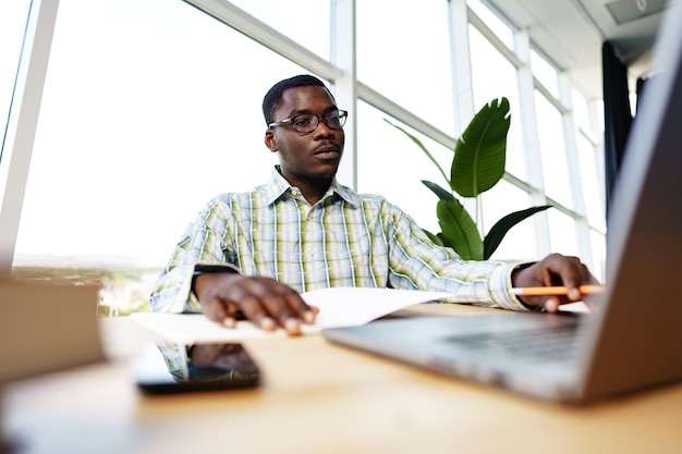 Serious concentrated african man studying or working with laptop indoors