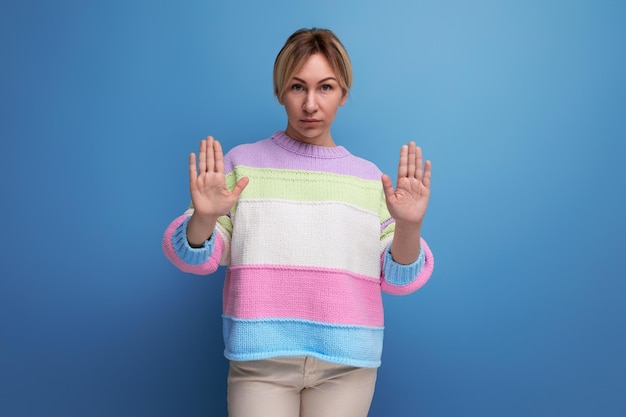 Serious concentrated blond young woman showing stop sign with hand on blue background