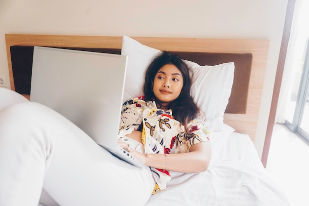 Serious concentrated young woman working from the bed Hold the laptop on the knees and type on the keyboard