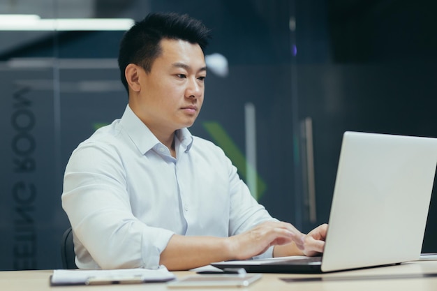 Serious and confident asian boss working in modern office businessman typing on laptop