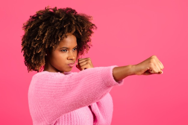 Serious confident young black curly female do hand punch isolated on pink background close up