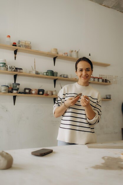 Photo serious creative female artisan standing at pottery workshop and making clay mug portrait of a focused artistic craftswoman standing at ceramics studio and making earthenwareartisan making clay mug