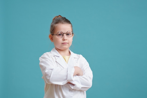 Serious cross-armed little girl in whitecoat and eyeglasses