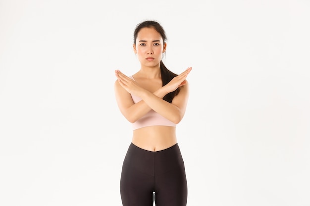 Serious and displeased frowning asian sportswoman show stop gesture, female fitness coach or instructor warning, restrict gym client