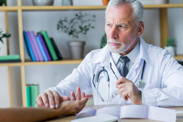 Serious doctor checking pulse of patient