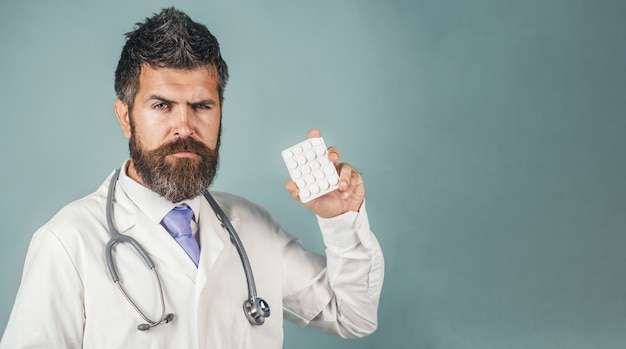 Serious doctor in white medical gown with stethoscope holds pills in hand Pharmacy and medicine