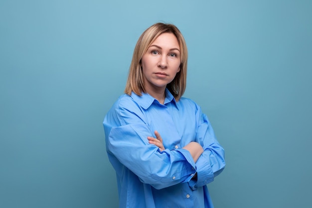 Serious european blond woman folded her hands in front of her on a blue background with copyspace